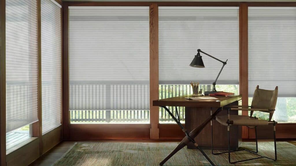 Light-filtering cellular blinds in a home office with wooden window frames, providing privacy and controlling sunlight with elegant window treatments.