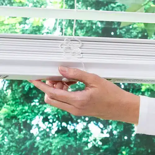Adjusting white window blinds with a hand, showcasing high-quality window treatments from Advance Blinds & Drapery.