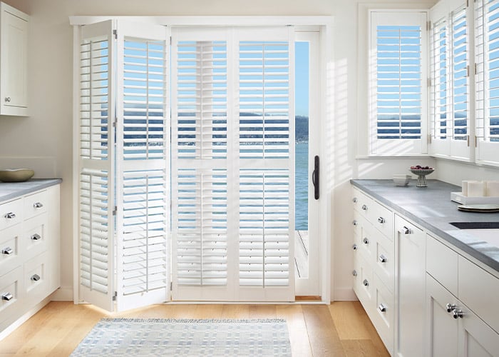 Custom white plantation shutters on sliding glass doors for enhanced privacy and light control in kitchens. Perfect window treatment solution from Advance Blinds & Drapery.