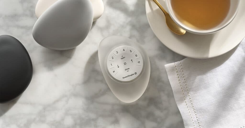 White egg-shaped smart home device with control buttons on marble surface, next to a cup of tea and decorative ceramic vases, emphasizing modern home automation solutions for comfort and convenience in interior design.