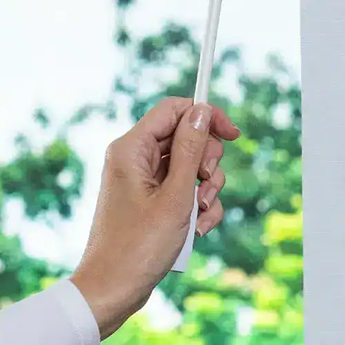 Highly detailed close-up of a hand adjusting window blinds, showcasing precision and quality, with a background of lush green trees and natural sunlight.