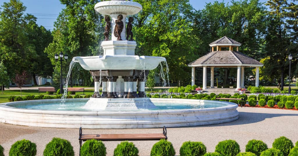 Elegant outdoor park with decorative fountain, lush greenery, and gazebo, showcasing beautiful landscape design perfect for outdoor living spaces.