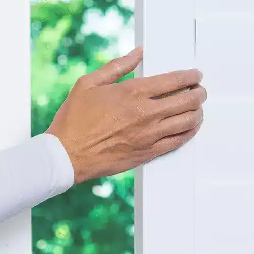 Soft-close window frame with a hand adjusting a white window treatment, showcasing high-quality blinds and drapery services.
