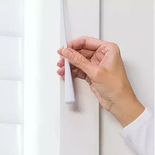 Roller shade installation being done with a hand holding a white window shade in a bright, modern home setting.