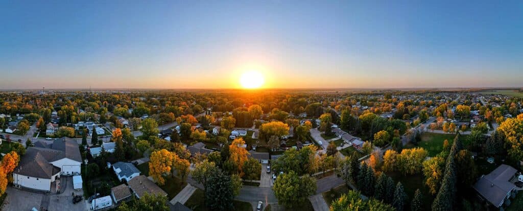 Vibrant aerial view of suburban neighborhood during sunset with lush green trees, showcasing home exteriors and residential streets, highlighting community and natural beauty for window treatments and home decor.