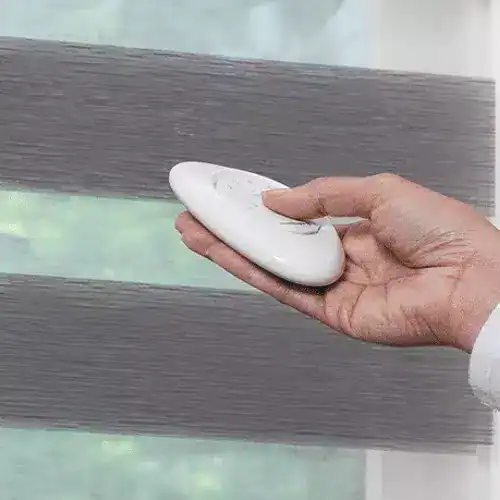 Soft gray window blinds being cleaned with a white cloth, showcasing professional window treatment services.