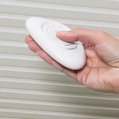 Adjustable remote control in hand for window blinds or shades, used to operate window coverings easily and conveniently.