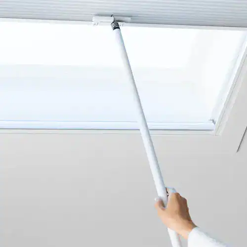 Extendable pole opening a skylight window with a white frame for easy access and natural light control.