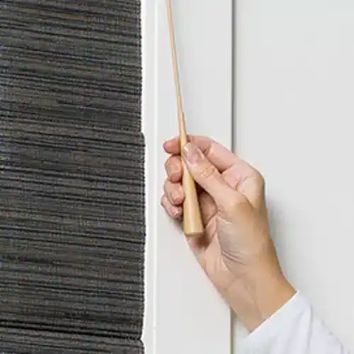 Wiping a black roller shade with a soft cloth to maintain its appearance and cleanliness, suitable for custom window treatment services.