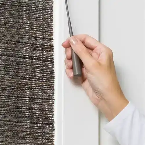 A person installing or adjusting a window blind or shade, demonstrating professional window treatment services.