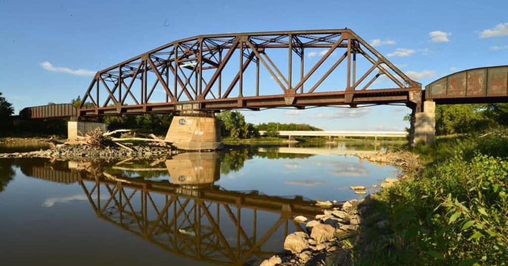 Iron bridge over river with clear blue sky and green landscape - historic steel truss bridge near waterway for home or commercial property decor.